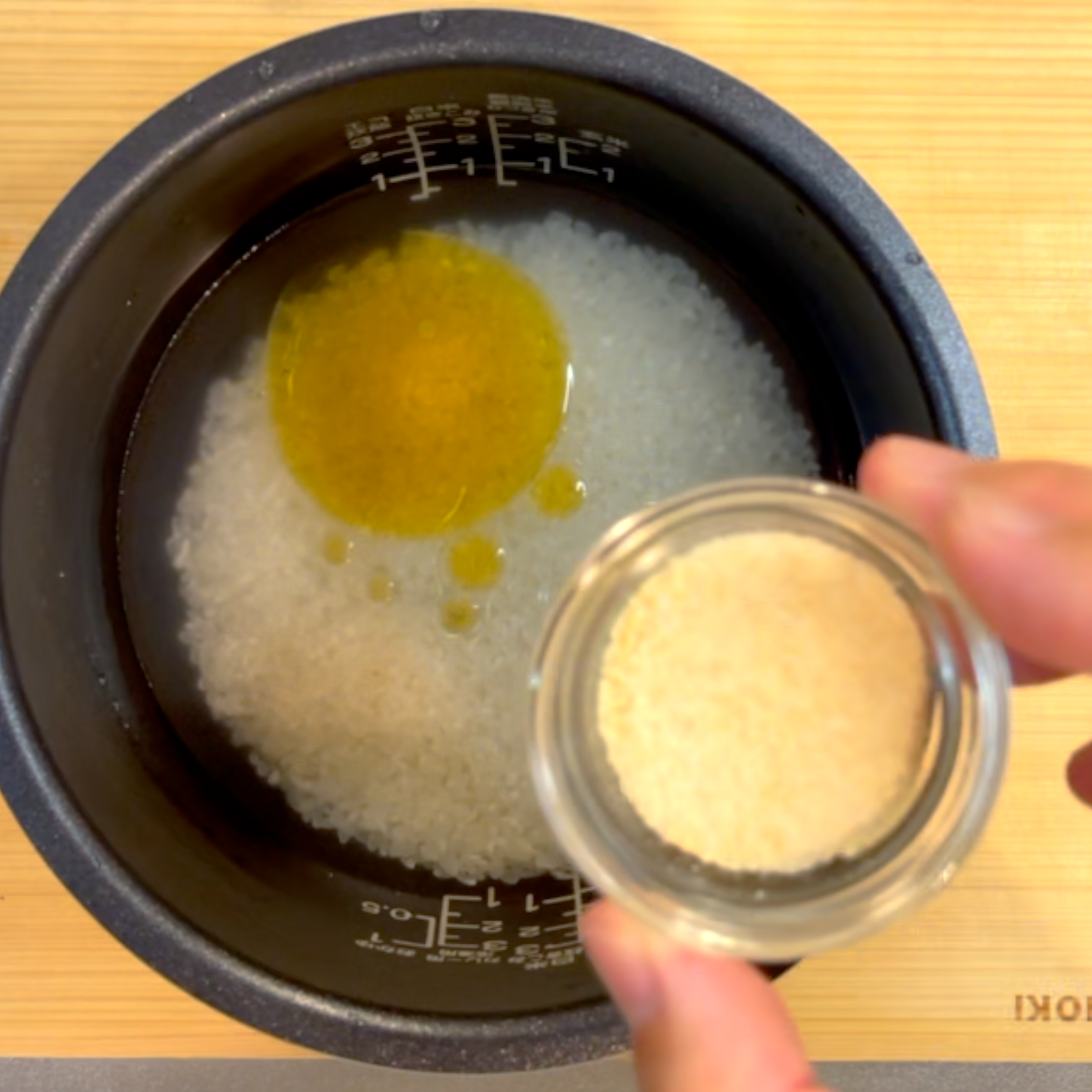 炊飯釜に洗った米と水、ごま油と鶏ガラスープのもとを入れて混ぜる様子