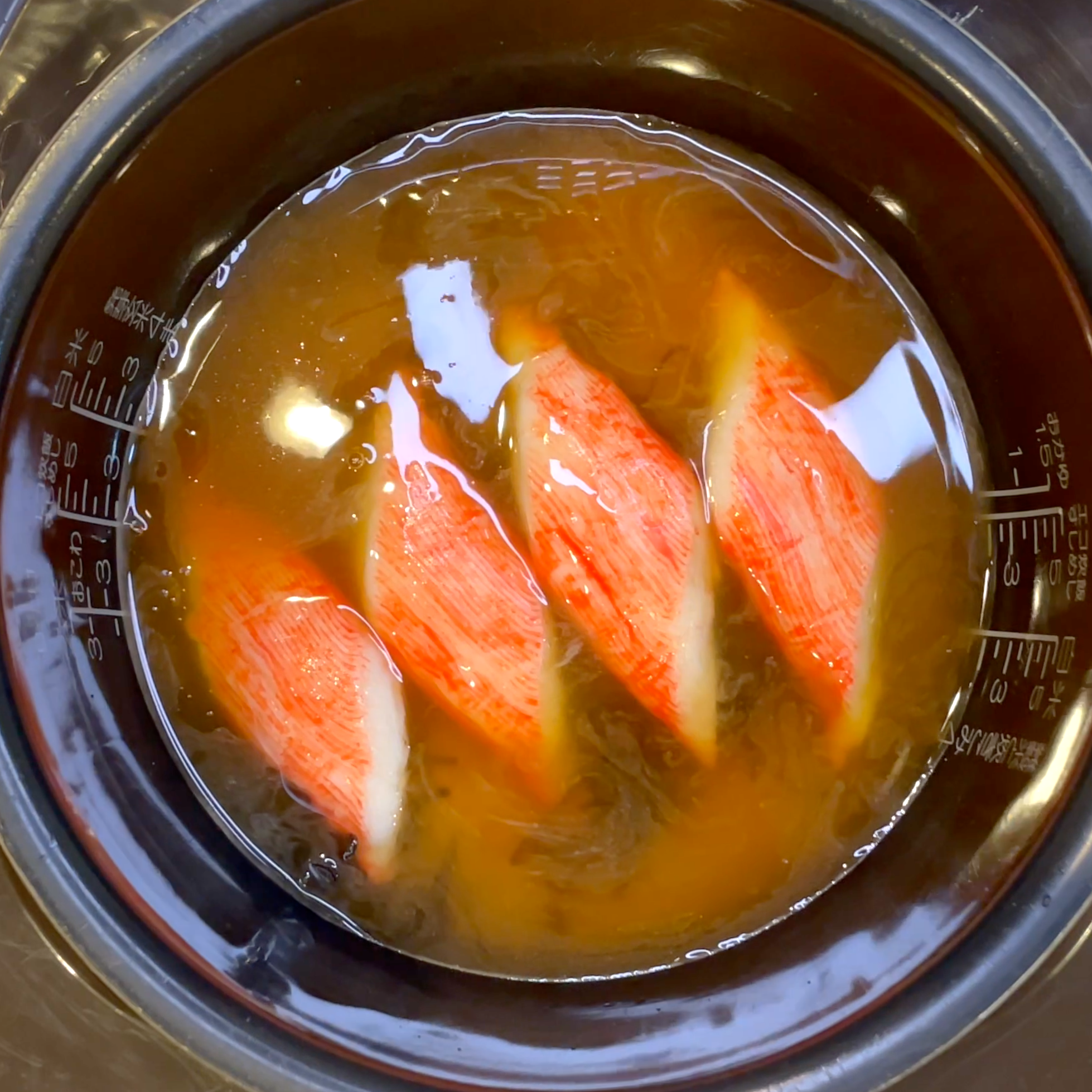 塩昆布とかにかまを米の上にのせて炊飯する工程