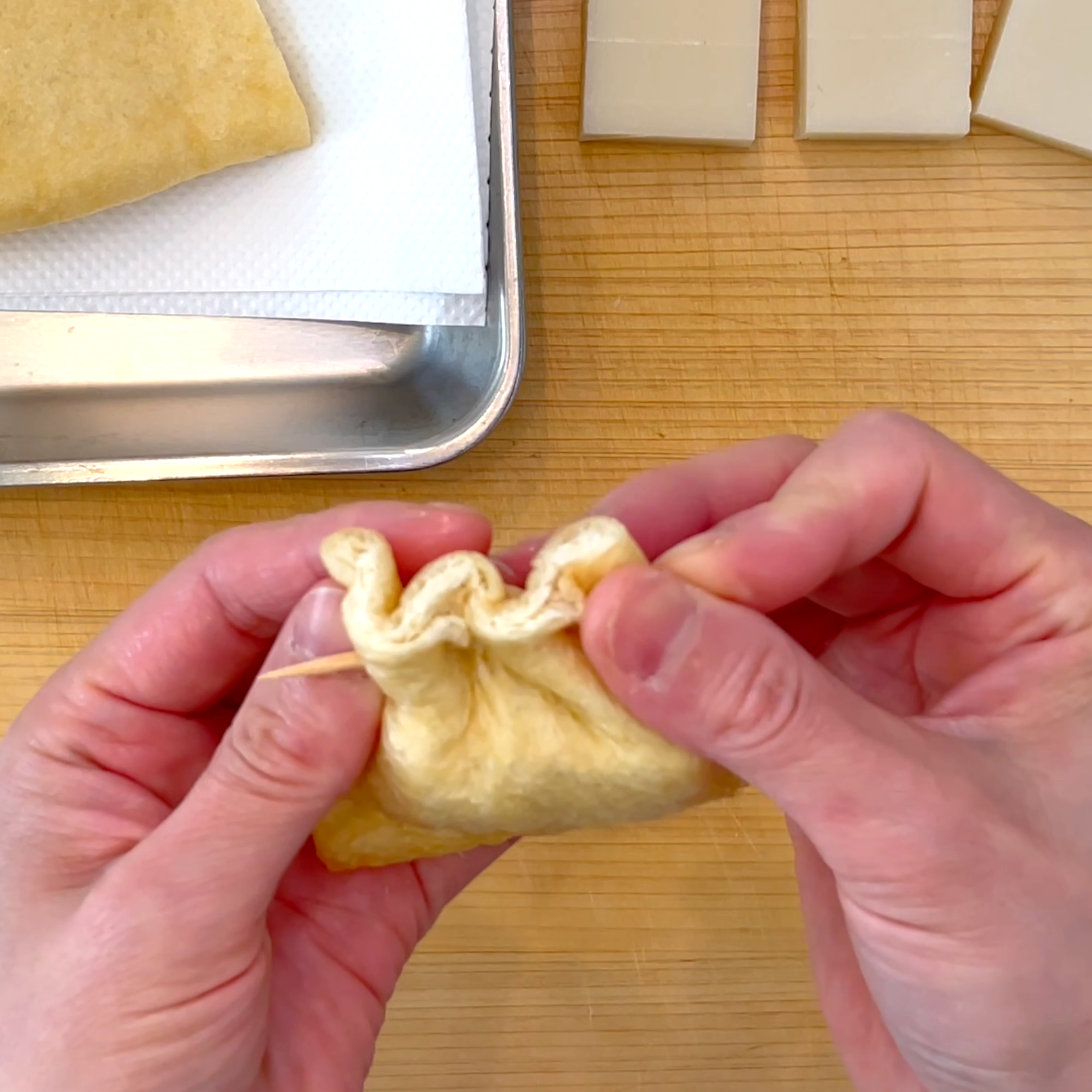 油揚げに餅を詰めて口を閉じる工程